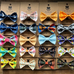 May include: A collection of twenty fabric bow ties attached to individual brown cardboard display cards. The bow ties feature various patterns including geometric shapes, floral prints, plaid, comic book graphics, and seasonal motifs in diverse colors.