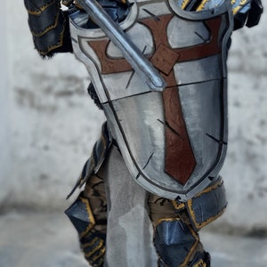 May include: A detailed costume of a medieval knight, featuring a silver and gold helmet with a cross emblem. The knight is clad in armor with a shield bearing a red cross, holding a sword. The costume has a weathered appearance.
