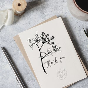 May include: A white card with a black line drawing of a flower and the text "thank you" written in cursive. The card also has a small circle with the text "Blue Moon" in cursive.