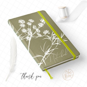 May include: A green notebook with a white floral design and a yellow elastic band. The notebook says "Notebook" on the cover. The text "Thank you" is written below the notebook. The text "Blue Moon" is written in a circle below the notebook.