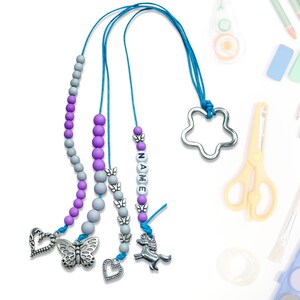 Może przedstawiać: Trzy kolorowe sznurki z koralików z zawieszkami. Sznurki są wykonane z szarych, fioletowych i niebieskich koralików. Zawieszki to motyl, serce, jednorożec i gwiazda. Sznurki idealnie nadają się do trzymania kluczy, odznak lub innych drobnych przedmiotów.