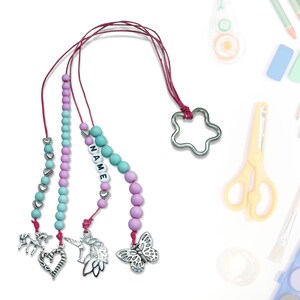 Może przedstawiać: Różowo-turkusowy sznurek z koralików z metalowym zawieszką w kształcie gwiazdy, zawieszką w kształcie jednorożca, zawieszką w kształcie wróżki i zawieszką w kształcie motyla. Sznurek ma napis "NAME" wyłożony białymi koralikami.