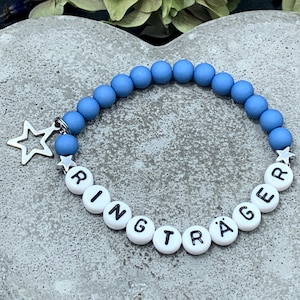 Könnte beinhalten: Ein blaues Perlenarmband mit weißen Perlen, die "Ringträger" buchstabieren, und einem silbernen Sternanhänger.