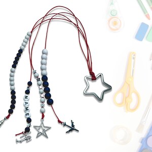Może przedstawiać: Cztery czerwone sznurki z niebieskimi i białymi koralikami, każdy z innym srebrnym wisiorkiem: gwiazdą, samolotem, helikopterem i etykietą z napisem "NAME".