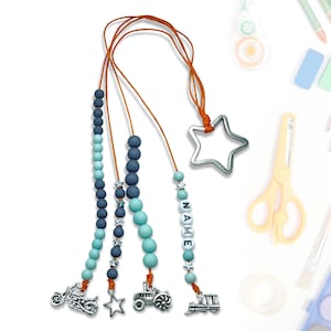 Może przedstawiać: Zestaw trzech niebieskich i turkusowych naszyjników z koralików z zawieszkami. Zawieszki obejmują motocykl, traktor i pociąg. Naszyjniki są nawleczone na brązowe sznurki i mają srebrną zawieszkę w kształcie gwiazdy na górze.