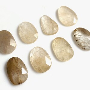 May include: Eight smooth, oval-shaped, light brown and white gemstone cabochons with a faceted edge.