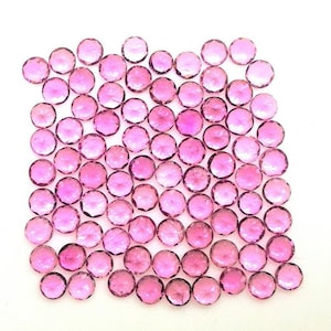 May include: A collection of round, faceted gemstones in varying shades of pink. The gemstones are scattered across a white surface, each displaying a brilliant cut that catches the light. The overall effect is a display of sparkling, colorful gems.