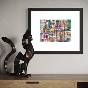 May include: A black framed abstract art print with a colorful grid pattern. A black cat sculpture with copper accents sits on a wooden cabinet. The artwork features intersecting lines in various colors.