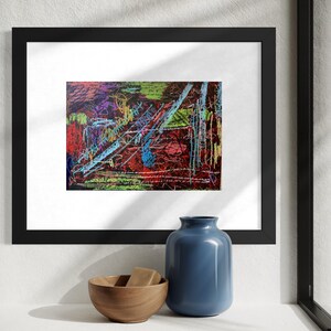 May include: Abstract art print in a black frame. The artwork features a vibrant mix of colors, including red, blue, green, and yellow, with a textured appearance. A blue vase and a wooden bowl are in the foreground.
