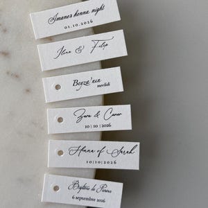 Pode incluir: Seis etiquetas retangulares de papel branco com texto impresso em preto em várias fontes. As etiquetas apresentam nomes e datas, incluindo Imane's henna night, Ilona & Filip, Beyza'nun mevlidi, Zara & Caner, Henna of Sarah e Bapteme de Pierina.