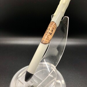 May include: White pen with a black tip and a wax-like drip design. The pen has a label that reads "Salem, MA.  Black Flame Candle Co.  Extraordinary Scents Since 1908."