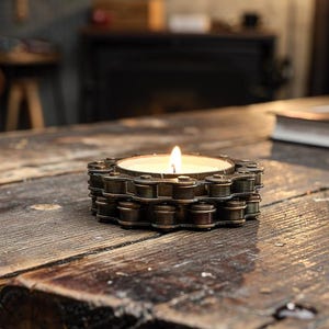 Può includere: Una candela accesa in un portacandele unico realizzato con maglie di catena di bicicletta in metallo riciclato. Il portacandele è appoggiato su un tavolo di legno rustico e invecchiato. La luce calda della fiamma contrasta con il metallo freddo.