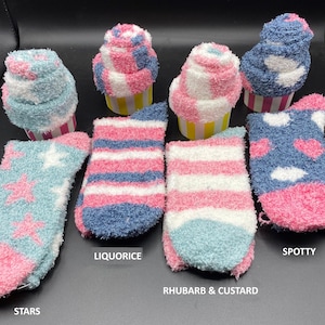 May include: A collection of fluffy socks in various designs and colors, including light blue with pink stars, pink and blue stripes, and blue with pink hearts. The socks are arranged with cupcake-shaped items.