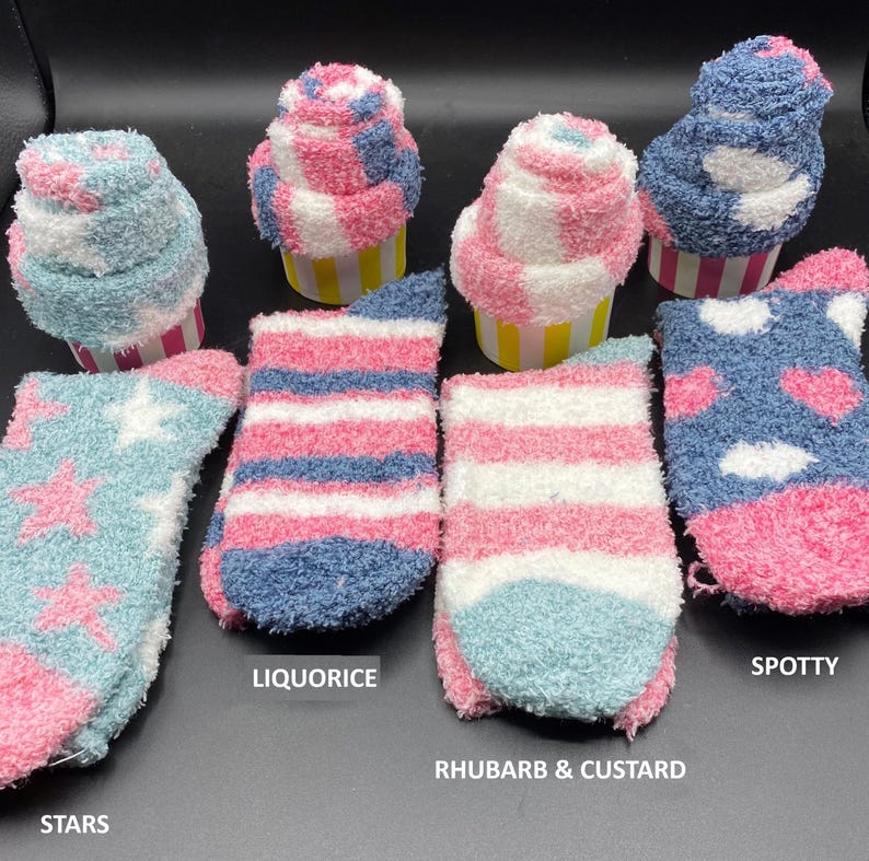 May include: A collection of fluffy socks in various designs and colors, including light blue with pink stars, pink and blue stripes, and blue with pink hearts. The socks are arranged with cupcake-shaped items.