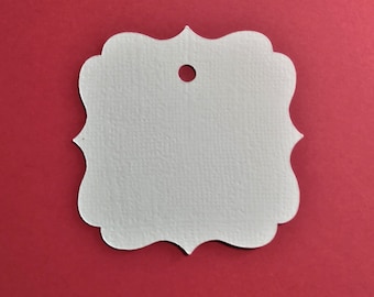 May include: A white, ornate-edged tag with a small hole at the top center. The tag has a textured surface and is set against a solid red background. Ideal for crafting or gift-giving.