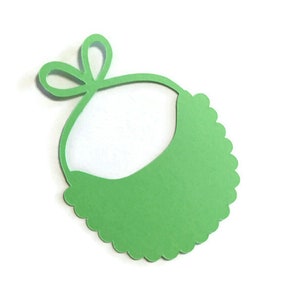 May include: A green paper bib with a scalloped edge and a bow at the top. The bib is cut out and ready to be used for a craft project.