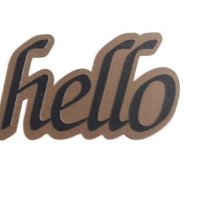 May include: A brown paper cutout of the word "hello" in a cursive font with black lettering.