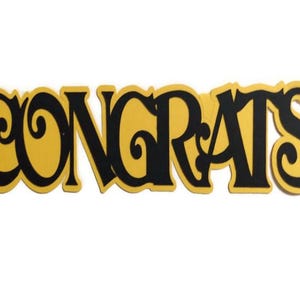 May include: A yellow and black paper cutout of the word "CONGRATS" in a decorative font.