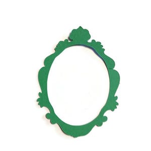 May include: A flat, die-cut paper cutout in the shape of an ornate oval picture frame. The frame is a solid, vibrant green color with decorative, scalloped edges and a small, pointed crest at the top center, featuring a hollow, empty oval center.
