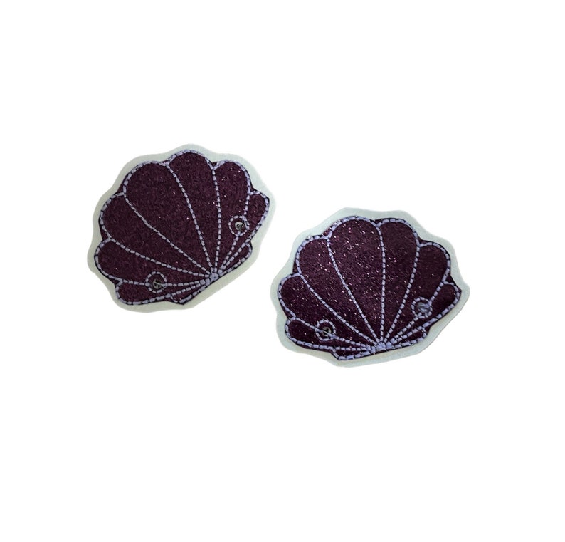 May include: Two purple glitter seashell patches with white stitching and a pearl-like embellishment on each.