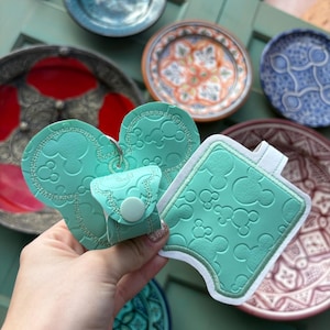 May include: Two turquoise blue Mickey Mouse-shaped hand sanitizer holders. One holder is a keychain with a snap closure. The other holder is a flat, rectangular shape with a stitched border.