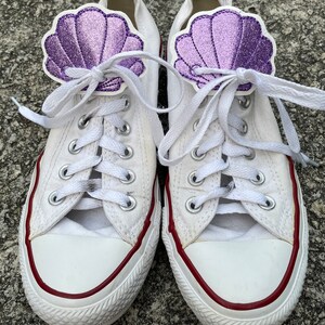 May include: White canvas sneakers with red trim and purple glitter seashell shoe laces.