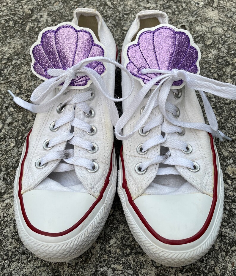May include: White canvas sneakers with red trim and purple glitter seashell shoe laces.