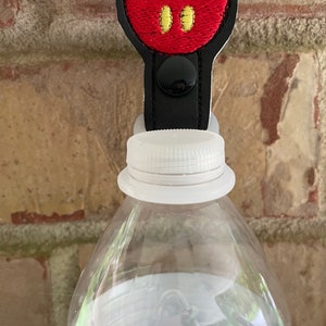 May include: Black and red Mickey Mouse character bottle stopper with a black button. The stopper is attached to a clear plastic water bottle.