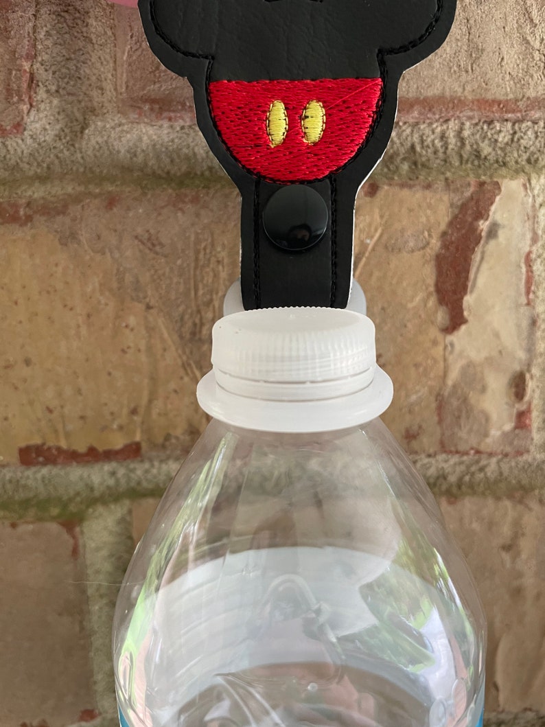 May include: Black and red Mickey Mouse character bottle stopper with a black button. The stopper is attached to a clear plastic water bottle.