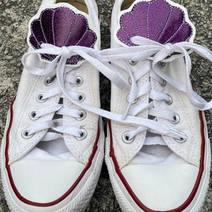 May include: White canvas sneakers with red trim and purple glitter seashell shoe charms.