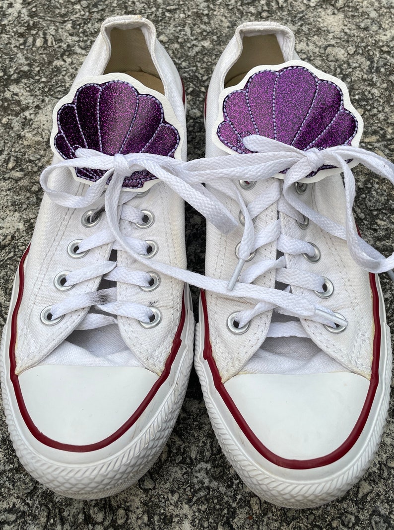 May include: White canvas sneakers with red trim and purple glitter seashell shoe charms.