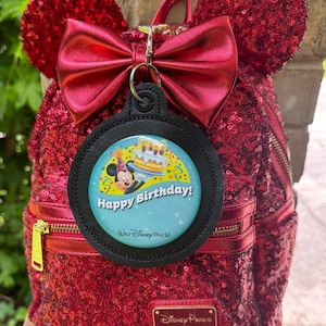 May include: Red sequined backpack with Mickey Mouse ears and a red bow. A circular tag with "Happy Birthday!" text and a Mickey Mouse graphic is attached. The backpack has gold zips and a Disney Parks Loungefly label.