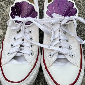May include: A pair of white canvas sneakers with red trim and purple glitter seashell shoe charms.