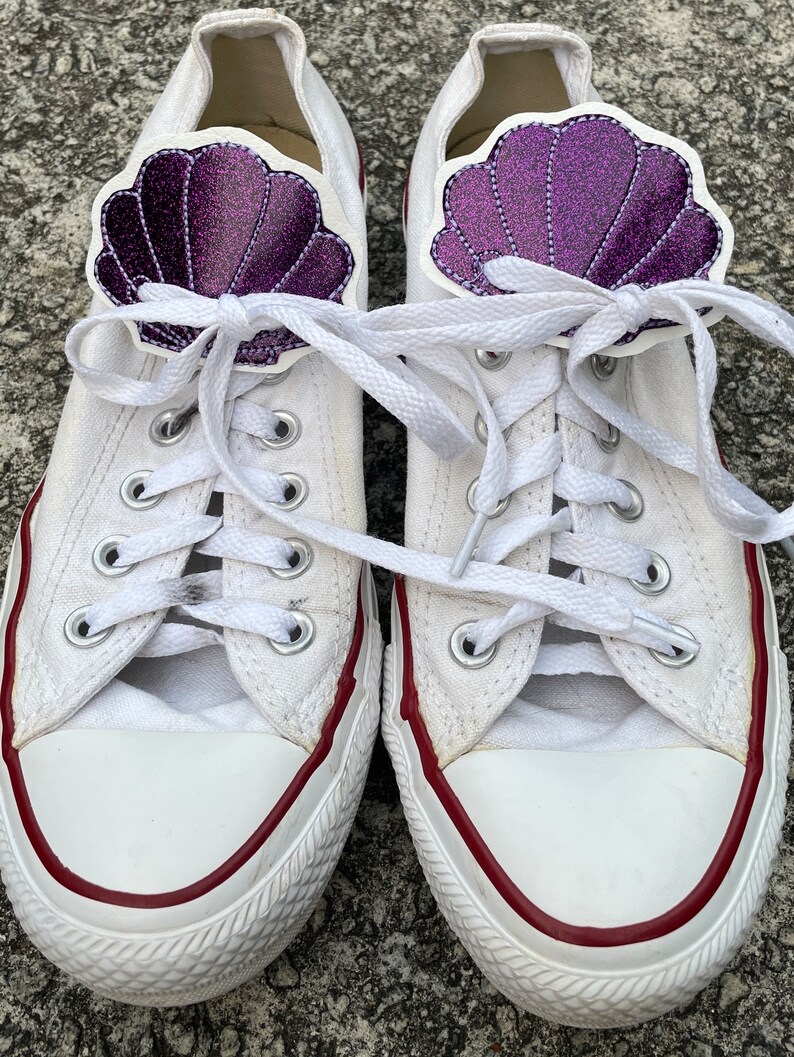 May include: A pair of white canvas sneakers with red trim and purple glitter seashell shoe charms.