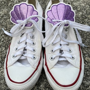 May include: White canvas sneakers with red trim and purple glitter seashell embellishments on the laces.
