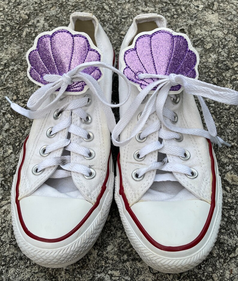 May include: White canvas sneakers with red trim and purple glitter seashell embellishments on the laces.