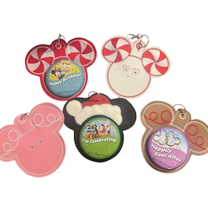 May include: Five different Disney-themed pin trading lanyards. Each lanyard features a different design with a Mickey Mouse ear shape. The designs include a red and white candy cane, a white and red candy cane, a brown and white reindeer, a pink and white Mickey Mouse, and a brown and white Mickey Mouse. Each lanyard has a pin holder in the center with a different design. The pins include a "Happy Birthday" pin, an "I'm Celebrating" pin, a "Happily Ever After" pin, and two other pins with Mickey Mouse designs.
