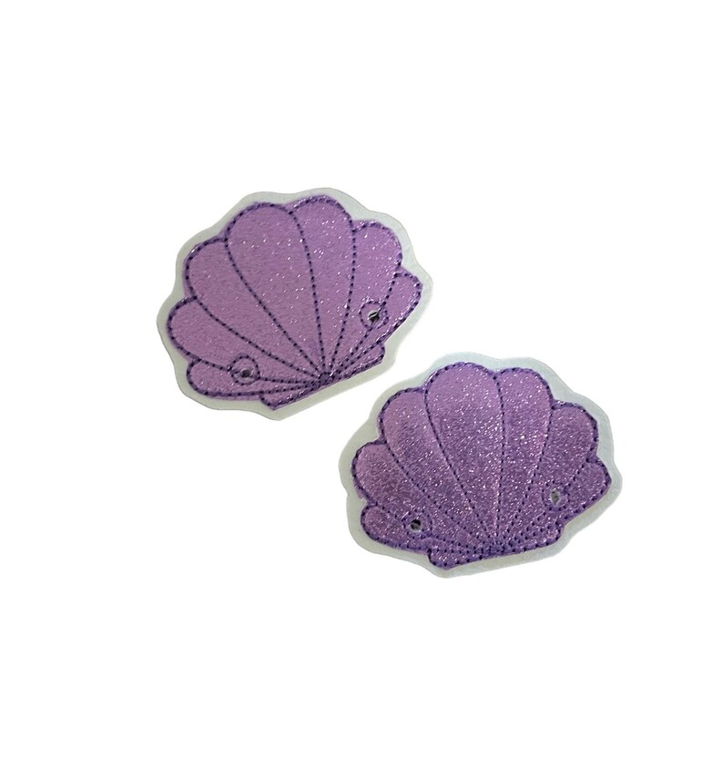 May include: Two purple glitter seashell patches with white outlines. The seashells are embroidered with a detailed design.