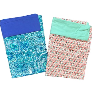 May include: Two folded fabric items. One has a blue top and a turquoise and white floral pattern. The other has a mint green top and a geometric pattern in red, white, and teal. Both items are on a white background.