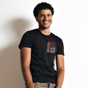 May include: A man wearing a black t-shirt with a red, white, and blue American flag graphic on the front. The flag is distressed and has a red axe superimposed on it.