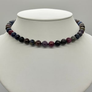 May include: A necklace made of dark blue, purple, and pink gemstone beads. The beads are round and have a smooth, polished finish.