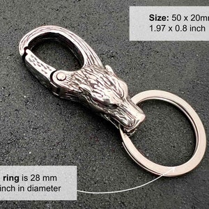 May include: A silver-colored keychain with a wolf head design. The keychain has a clasp and a ring. The ring is 1.1 inches in diameter. The keychain is 1.97 x 0.8 inches. The text on the image says "The ring is 28 mm 1.1 inch in diameter" and "Size: 50 x 20mm 1.97 x 0.8 inch".