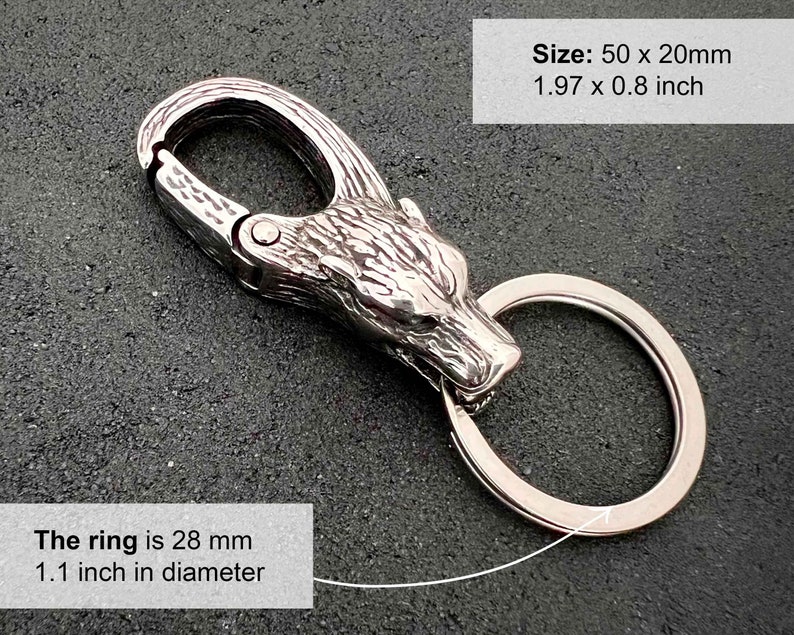 May include: A silver-colored keychain with a wolf head design. The keychain has a clasp and a ring. The ring is 1.1 inches in diameter. The keychain is 1.97 x 0.8 inches. The text on the image says "The ring is 28 mm 1.1 inch in diameter" and "Size: 50 x 20mm 1.97 x 0.8 inch".