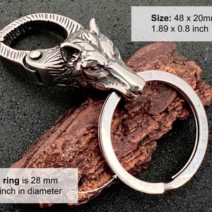 May include: A silver-colored keychain featuring a wolf head design. The keychain includes a large ring and a clasp. The wolf head is intricately detailed. The keychain measures 1.89 x 0.8 inches (48 x 20mm), with a ring diameter of 1.1 inches (28 mm).