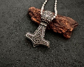 May include: A silver Mjolnir pendant necklace with intricate detailing and a beaded chain. The pendant features a detailed design of the hammer of Thor, a Norse god.