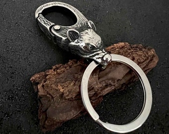 May include: A silver wolf head keychain with a large ring. The wolf's head is detailed and realistic, with sharp teeth and a fierce expression.