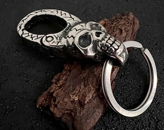 May include: A silver skull keychain with a detailed design and a swiveling clasp. The keychain is attached to a silver ring.