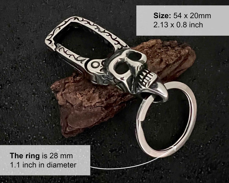 Puede incluir: Un llavero plateado con dise&ntilde;o de calavera y un anillo grande. El llavero mide 54 x 20 mm, y el anillo tiene un di&aacute;metro de 28 mm. El texto de la imagen dice "Size: 54 x 20mm 2.13 x 0.8 inch" y "The ring is 28 mm 1.1 inch in diameter."