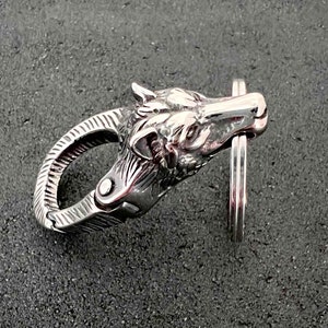 May include: A silver-colored keychain clasp in the shape of a wolf's head. The clasp is highly detailed, with visible fur and facial features. The clasp is attached to a silver key ring.
