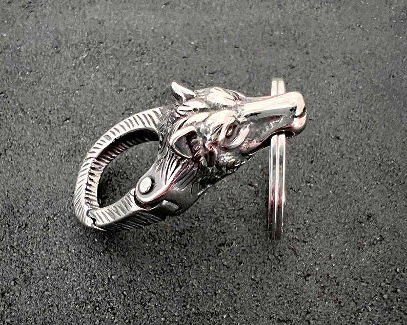 May include: A silver-colored keychain clasp in the shape of a wolf's head. The clasp is highly detailed, with visible fur and facial features. The clasp is attached to a silver key ring.